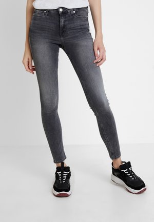 Úzké vybledlé černé džíny nošené s černo-bílými výraznými teniskami, zobrazené na stojící osobě od pasu dolů.