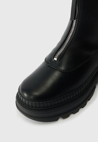 Melnas ādas potītes zābaki ar noapaļotu purngali, ar rāvējslēdzēju un teksturētu gumijas zoli, ar izcilām šuvēm gar malu un matētu apdari.