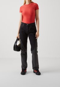 Rød tætsiddende t-shirt, højtaljede sorte jeans med tonal lapdetaljer, og sort taske med guldlister. Sorte sneakers med røde accenter.