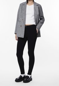 Grey plaid double-breasted blazer over a white fitted top, paired with black slim-fit jeans and black loafers with thick soles.