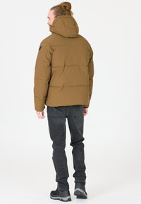 Brun, fyldig jakke med hætte, der har et quiltet design. Bæres med mørkegrå jeans og sorte vandrestøvler. Enkel, funktionel stil.