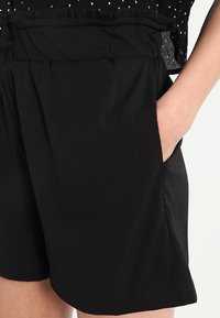 Black shorts with a drawstring waist, side pockets, and a lightweight fabric. The design features a smooth texture and relaxed fit.
