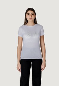 Maglietta bianca in cotone con maniche corte, caratterizzata da una stampa grafica argentata lucida sul davanti. Tessuto liscio, design con scollo tondo.