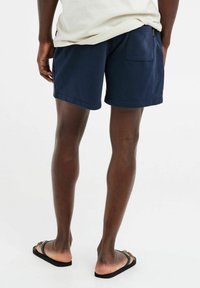 Marineblauwe short met een zachte textuur, voorzien van een achterzak en een casual fit, gecombineerd met zwarte slippers.