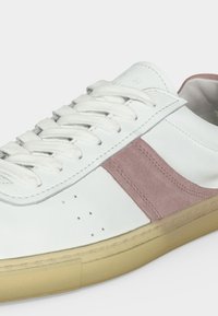 Baskets en cuir blanc avec bande latérale en daim rose et semelle en caoutchouc beige, montrant les lacets et les détails de couture.