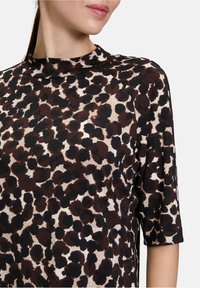 Brązowa i kremowa bluzka w zwierzęcy wzór z wysoką szyją, krótkimi rękawami i miękką fakturą, charakteryzująca się luźnym i casualowym stylem.