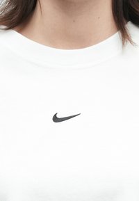 Rövid barna haj, ami a nyak fölött látható, fehér ing, amelyen a mellkas közepén egy kis fekete Nike logo található