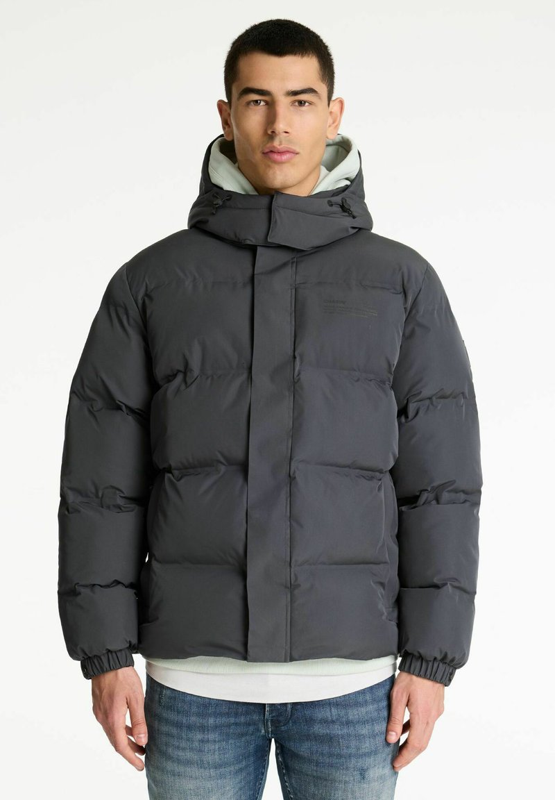 Svart puffjacka med hög krage och justerbar huva; har stygnpaneler och elastiska cuffs, bärs över en ljusgrå hoodie.