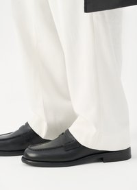 Mustad musta nahast loafers, millel on kootud detailid, kombineeritud valgete pükstega. Kingad omavad ümarat ninaosa ja madalat kontsa. Puhtad, minimalistlikud jooned.