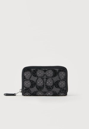 Portefeuille noir à fermeture éclair avec un motif texturé de petites perles formant des formes géométriques sur un fond en tissu gris.