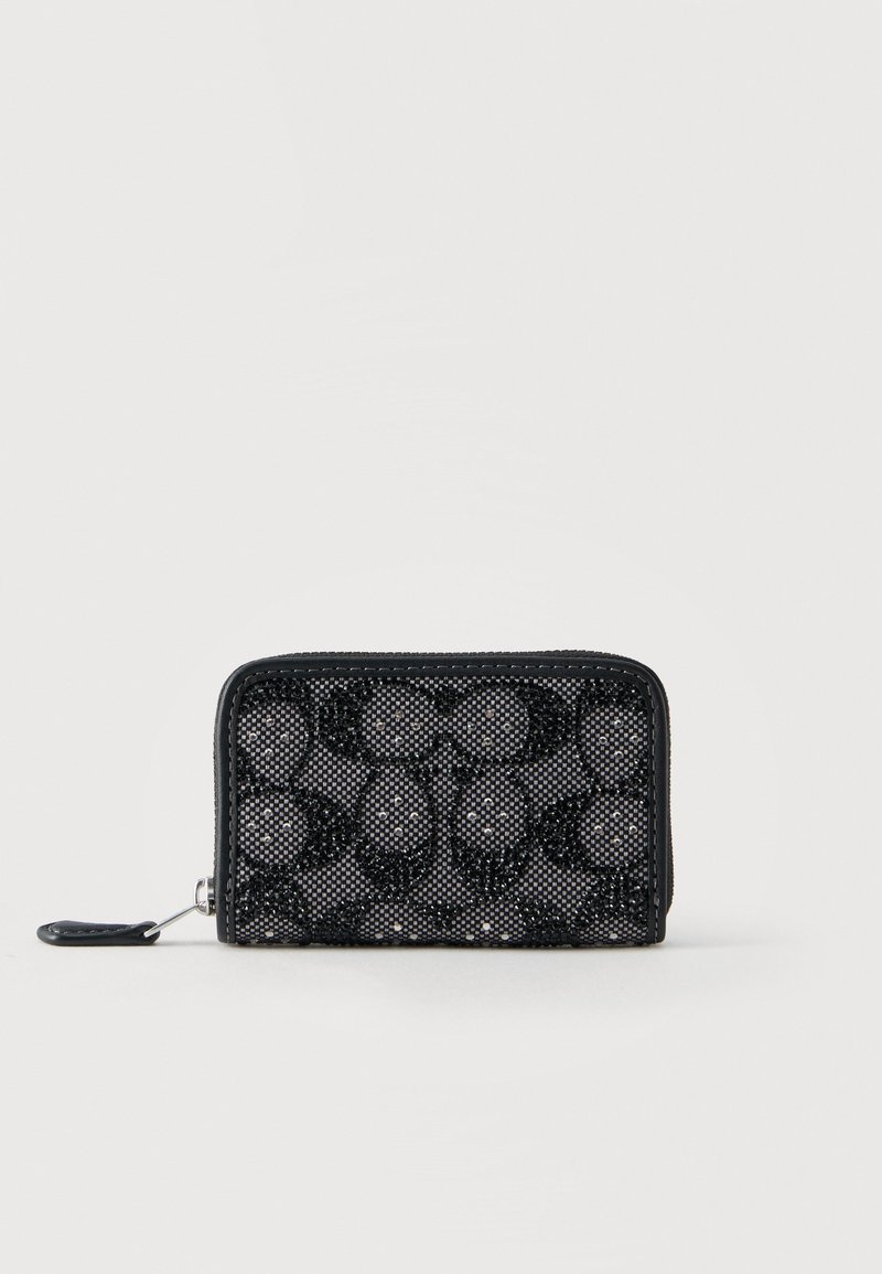 Μαύρο πορτοφόλι με φερμουάρ και υφή από μικρές χάντρες που σχηματίζουν γεωμετρικά σχέδια πάνω σε γκρι υφασμάτινο φόντο.