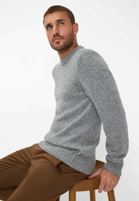 Grauer Wollpullover mit rundem Halsausschnitt und gerippten Bündchen, der ein strukturiertes Muster aufweist und ein kleines Etikett am Saum hat.