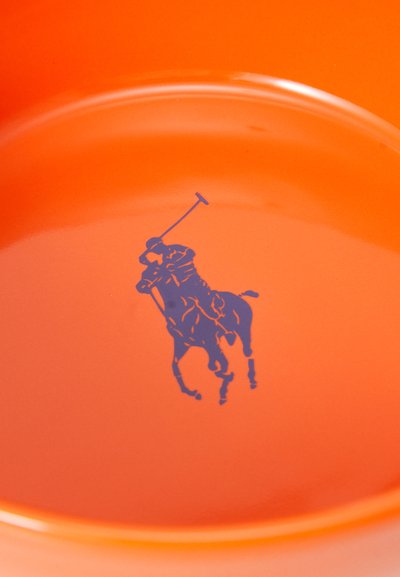 Apaļa oranža keramikas šķīvis ar gludu apdari, centrā ir zils polo spēlētāja logo. Gluda tekstūra un tīrs dizains.