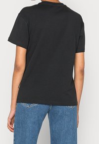 Sort bomulds t-shirt med rund hals og korte ærmer, med lige skæring og et lille mærke på venstre side nær kanten.