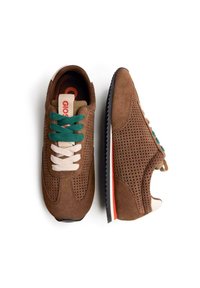 Baskets en suede marron avec des côtés perforés, dotées de lacets verts et crème, d'une étiquette logo rouge et d'une semelle en caoutchouc noir avec un accent orange.