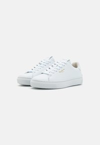 Zapatillas de cuero blanco con un acabado suave, diseño de cordones, cuello acolchado y una suela de goma texturizada que presenta un sutil logo de la marca en dorado.