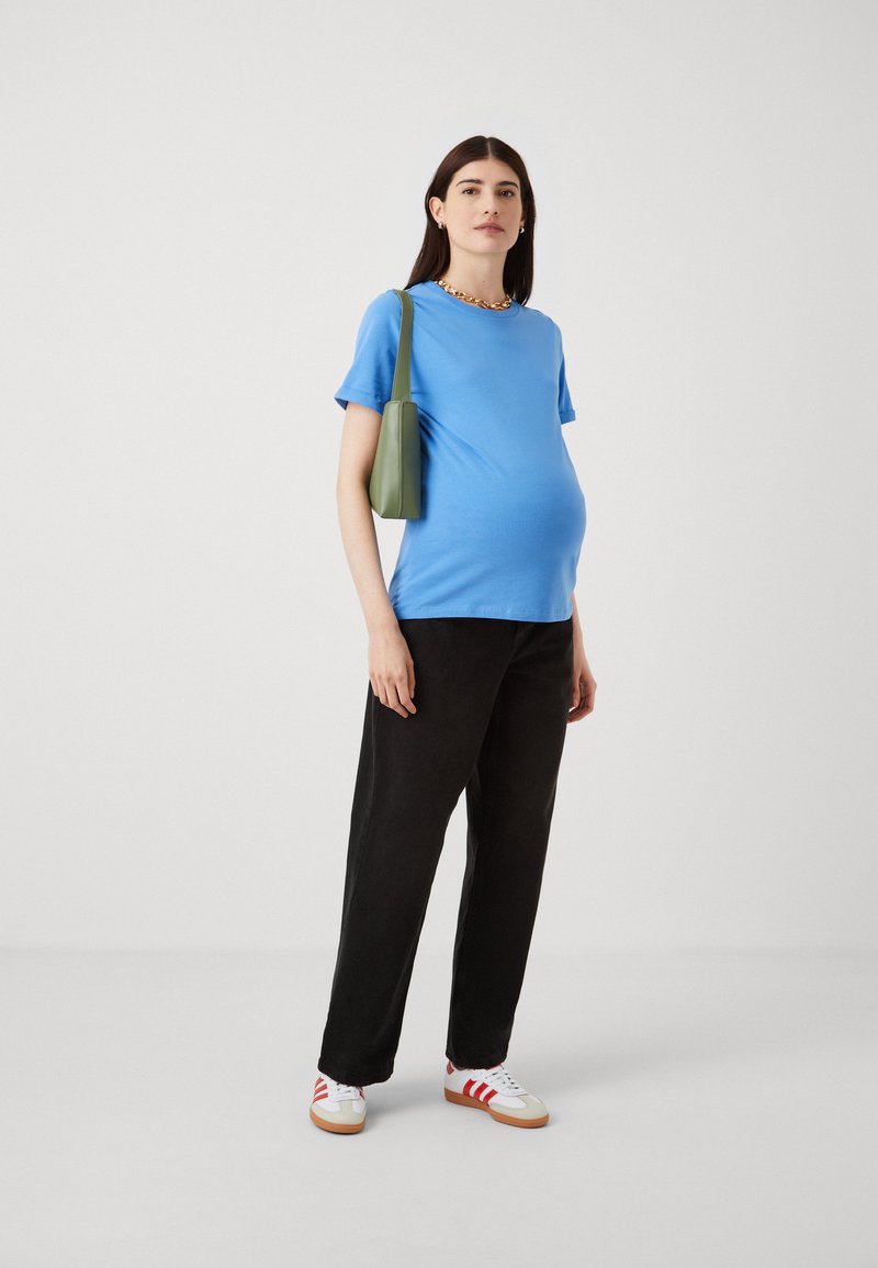 Lichtblauw katoenen T-shirt, korte mouwen, losse pasvorm; gecombineerd met zwarte wijde broek en witte schoenen met rode strepen. Groene schoudertas.