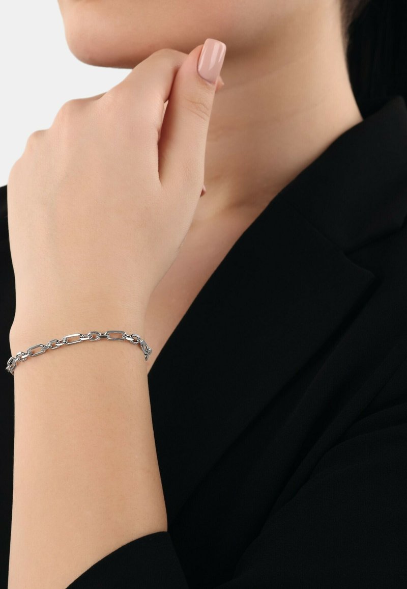 Pulsera de cadena de plata con formas ovaladas y rectangulares enlazadas, llevada en una muñeca, sobre un fondo de prenda negra.