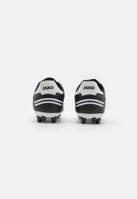 Botas de fútbol en blanco y negro con un acabado de cuero suave. Incluyen tres rayas blancas y el nombre de la marca "JAKO" en el talón. Suela texturizada.