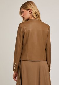 Brązowa skórzana kurtka o dopasowanym kroju, z długimi rękawami i guzikami przy mankietach. Gładka tekstura i minimalistyczny styl z czystymi liniami.