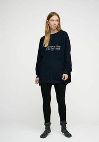 Felpa blu navy a maniche lunghe e dal fit rilassato, con testo bianco sul davanti. Abbinata a leggings neri e calze grigie a trama.