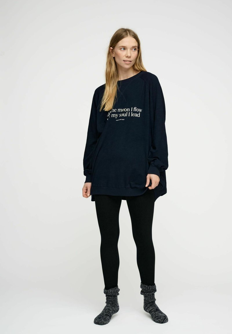 Felpa blu navy a maniche lunghe e dal fit rilassato, con testo bianco sul davanti. Abbinata a leggings neri e calze grigie a trama.