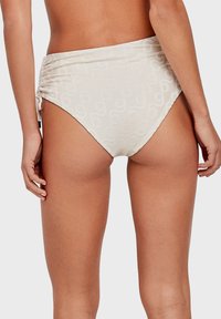 High-waisted bikini onderstuk in licht beige met een gestructureerd patroon. Kenmerkt zich door geplooide zijkanten voor een verstelbare pasvorm. Glad stofoppervlak.