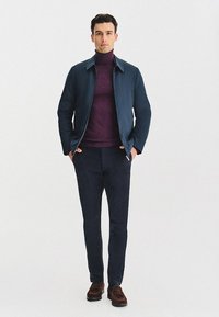 Marynarka w kolorze granatowym z zipem z przodu, w połączeniu z bordo golfem i ciemnymi spodniami. Brązowe loafersy dopełniają stylizację. Gładki materiał i dopasowany krój.