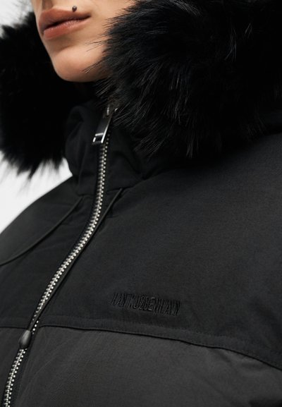 Μαύρο μπουφάν με κουκούλα με γούνα, δομημένο σχέδιο και εμφανές φερμουάρ κλεισίματος. Διακριτική επωνυμία στο στήθος. Απαλή υφή.