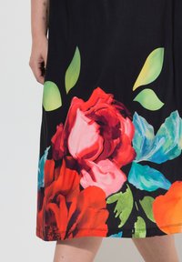 Kwiecista sukienka z czarnym tłem, na którym znajdują się duże różowe, czerwone i niebieskie kwiaty oraz zielone liście. Miękki materiał o żywych kolorach.