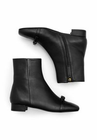 Botas de piel negra hasta el tobillo con punta afilada, cremallera lateral y un lazo decorativo. Textura suave y diseño de tacón bajo.