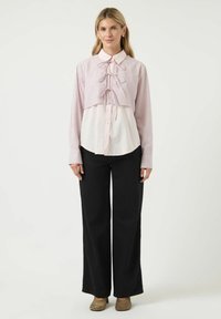 Randig kort topp i rosa och vitt med en knytning vid halsringningen, lagd över en vit långärmad skjorta, i kombination med svarta byxor.