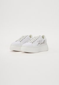 Sneakers bianchi in tela con suola in gomma spessa e testurizzata. Presentano lacci piatti e un dettaglio di perline che forma la scritta "Zal" sul lato.