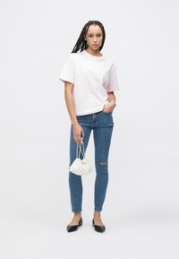 Ροζ βαμβακερό t-shirt με κοντά μανίκια, συνδυασμένο με στενά τζιν μπλε με σκισίματα. Το μοντέλο κρατά μια λευκή υφασμάτινη τσάντα και φοράει μαύρα φλατ παπούτσια.