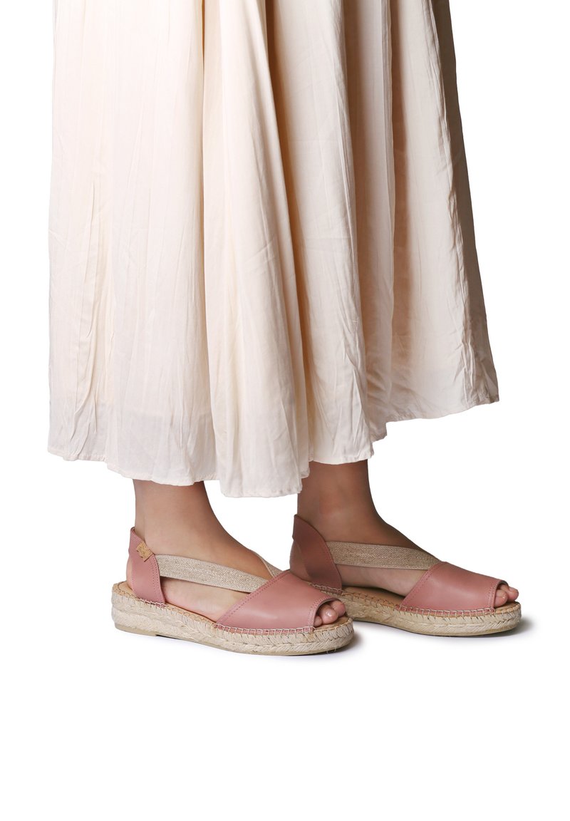 Sandales espadrilles en cuir rose avec bout ouvert, brides élastiques sur les côtés et semelle en jute tressé, assorties à une jupe fluide de couleur crème.