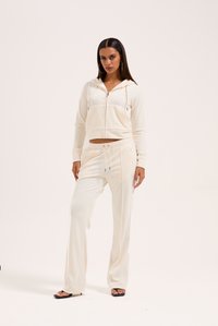 Set di loungewear color crema chiaro composto da una felpa cropped con zip e pantaloni a gamba larga, realizzato in tessuto morbido con vita regolabile e tasche decorative.