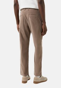 Brune bomuldstrusser med en lige pasform, der har to baglommer og matchende farvet syning. Brugt med lyse sneakers.