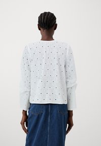 Λευκή μπλούζα με μακριά μανίκια, κυκλικά ανοίγματα και μαύρες λεπτομέρειες, συνδυασμένη με σιέλ τζιν φούστα με πίσω τσέπη και ίσια γραμμή.