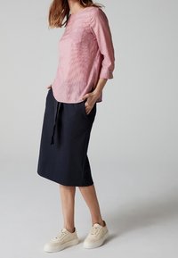 Ljusrosa texturerad blus med trekvartslång ärm, kombinerad med en knälång marinblå kjol och krämfärgade sneakers.