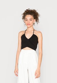 Top cropped preto estilo halter com decote em V, apresentando uma textura franzida e uma frente com nó. Usado com calças brancas de cintura alta.