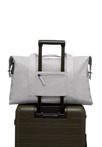 Sac de sport gris avec des poignées robustes, comportant une poche zippée à l'avant, reposant sur une valise rigide verte avec des poignées doubles extensibles.