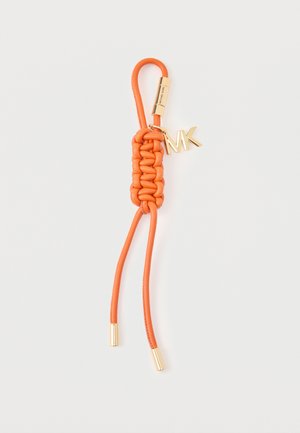 Porte-clés en cuir tressé orange avec des accents métalliques dorés et un pendentif logo MK suspendu sur un fond blanc.