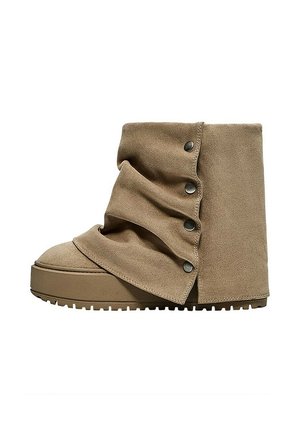 Bottine beige en daim avec un design plié et des boutons-pression métalliques sur le côté, avec une semelle épaisse en caoutchouc avec des crampons.
