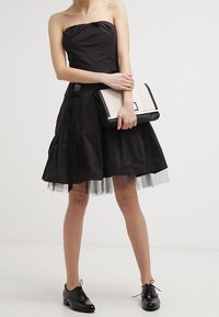 Robe noire sans bretelles avec un corsage ajusté et une jupe évasée, ornée de couches de tulle. Un sac à main noir et blanc apporte un contraste, assorti à des chaussures noires.