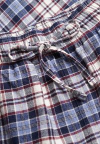 Cordon serré à la taille d'un tissu en flanelle à carreaux bleu, marine, blanc et rouge, montrant la texture tissée détaillée et le motif.