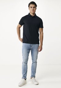 Svart polo skjorta av mjuk tyg, med krage och korta ärmar. Åtföljs av ljusblå jeans och vita sneakers.