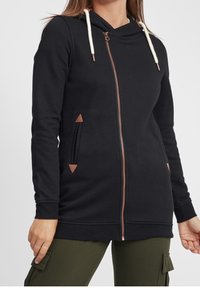 Felpa nera con zip realizzata in tessuto morbido, dotata di colletto a imbuto, cordino e dettagli in similpelle. Include due tasche laterali con dettaglio triangolare.