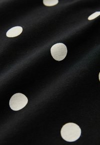 Black fabric with white polka dots, featuring a smooth texture and evenly spaced circular patterns across the surface.