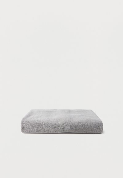 Διπλωμένη πετσέτα ανοιχτό γκρι, που βρίσκεται επίπεδη πάνω σε λευκή επιφάνεια με ομοιόμορφο ανοιχτό φόντο.