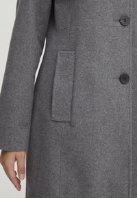 Manteau en laine gris avec une finition texturée, devant double boutonnage avec de grands boutons noirs, et poche latérale sur le côté gauche.